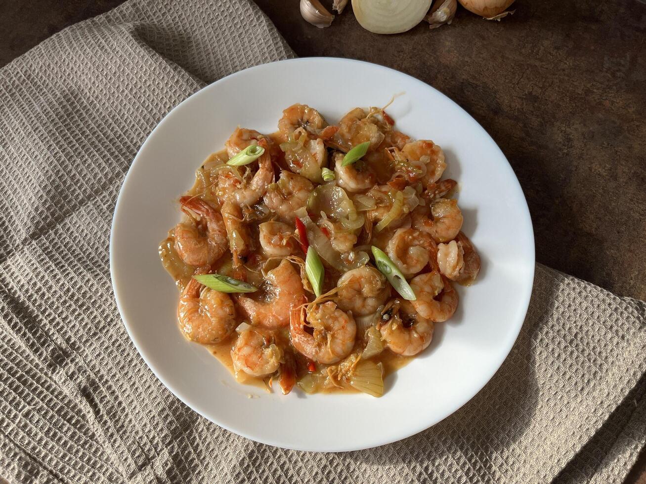Udang asam manis or Sweet and sour prawns, made from fried prawns with tomato sauce on white plate on dark background. Chinese food photo