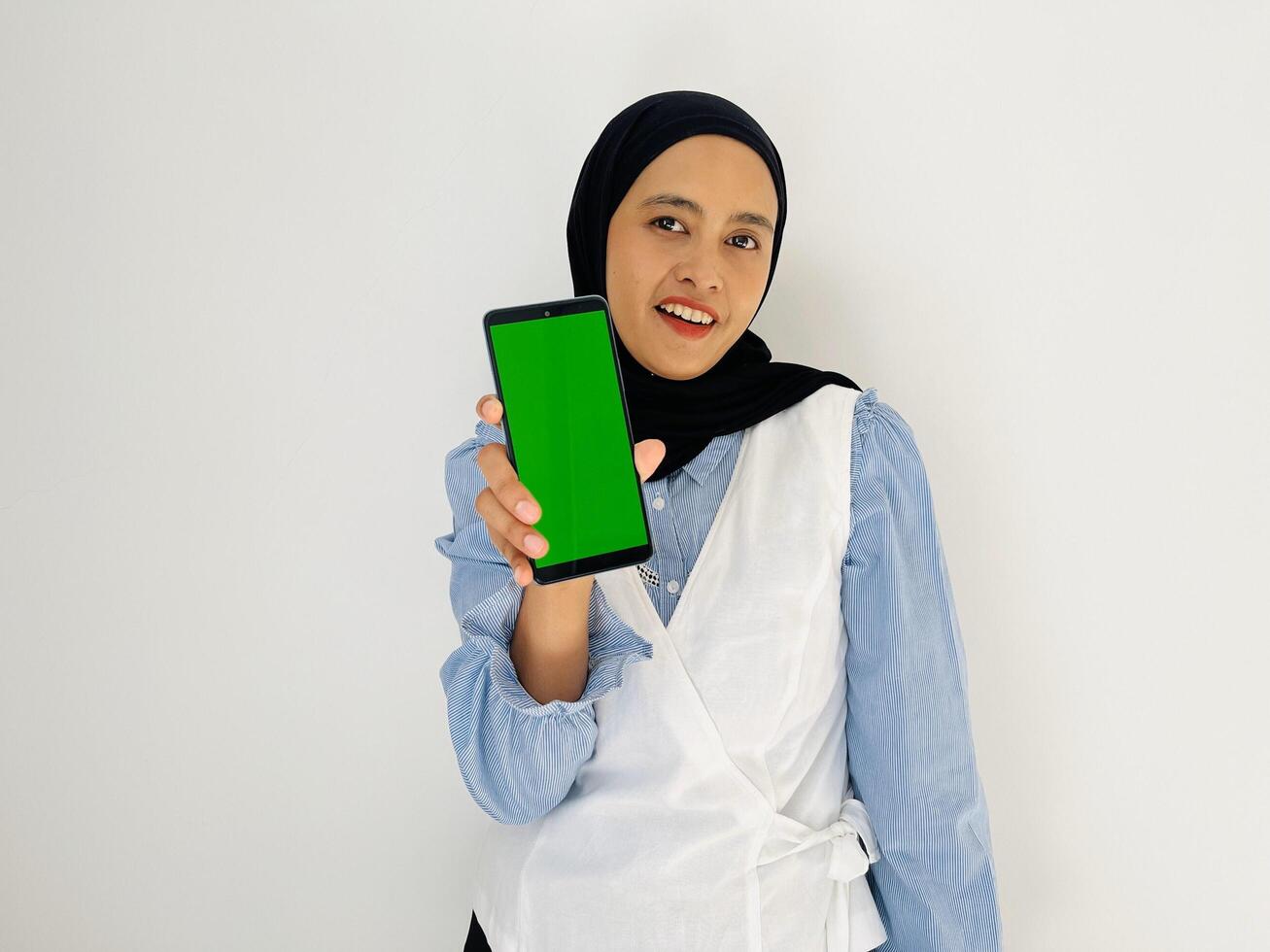 Indonesian woman holding mobile phone with green screen and looking at camera photo