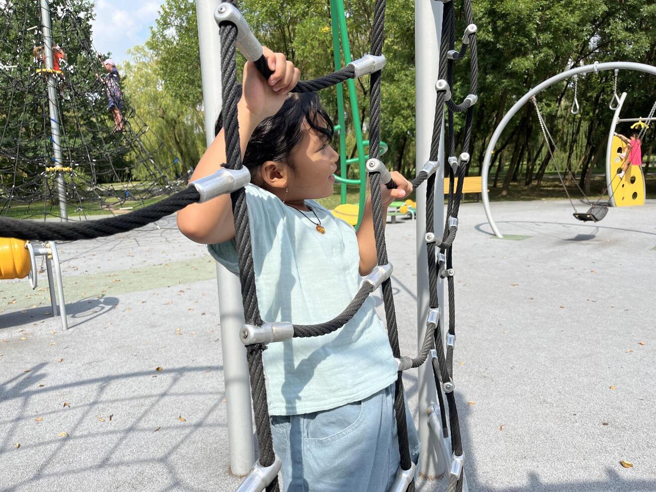 A young Asian little girl climbing on a rope in the playground. Happy kids concept. photo