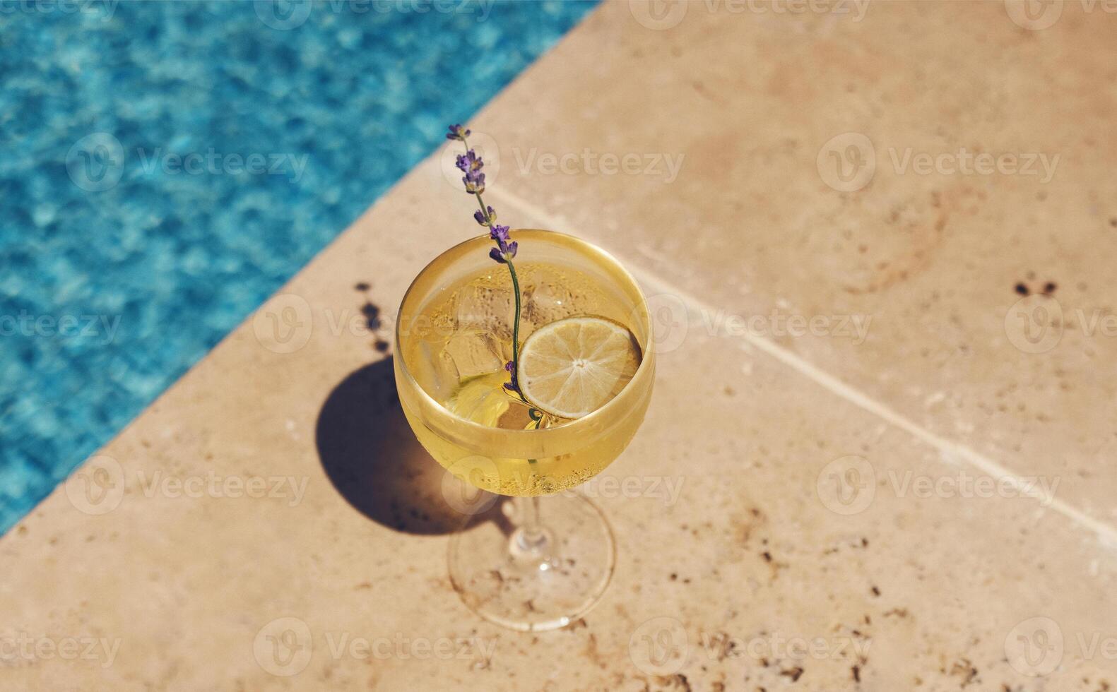 Elegant goblet of ice drink with lime slice and lavender on background of blue water photo