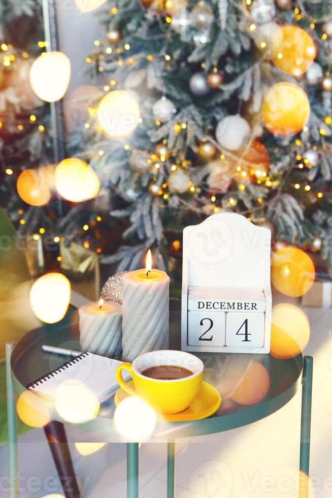 December 24 on wooden calendar standing on small table with burning candles in living room, selective focus. Christmas and New Year concept photo