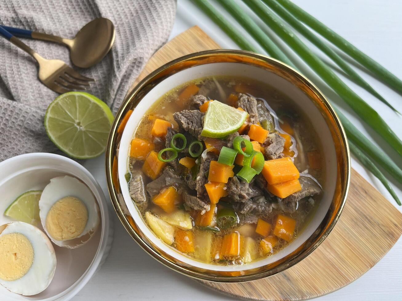 Beef soup is made from beef broth cooked with spices served with vegetables such as potatoes, carrots, spring onions, lime and boiled eggs. Perfect for articles, recipe books and creative production photo
