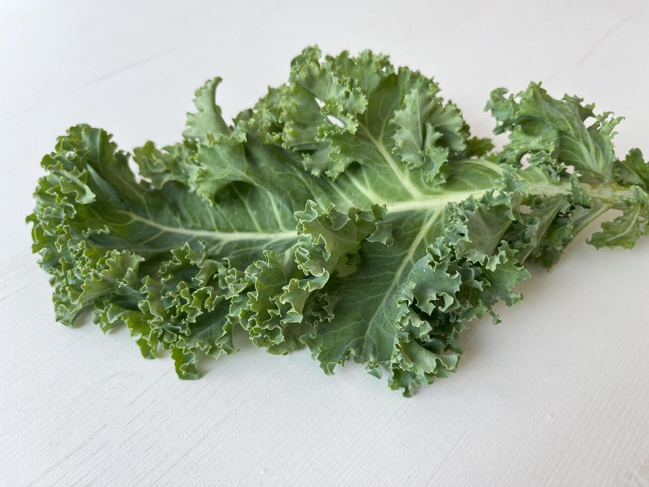 Kale leaf salad vegetable on white wooden table. Creative layout made of kale closeup. Food concept. photo