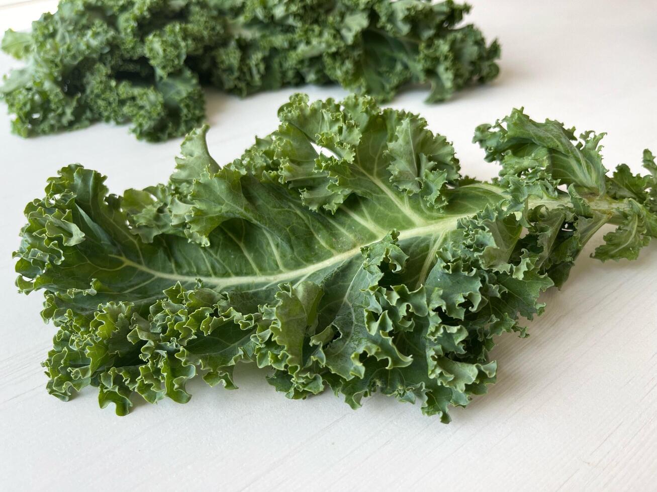 Kale leaf salad vegetable on white wooden table. Creative layout made of kale closeup. Food concept. photo