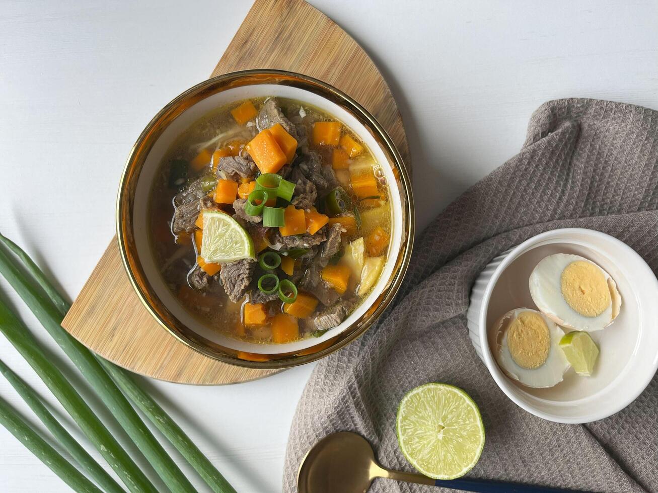 Beef soup is made from beef broth cooked with spices served with vegetables such as potatoes, carrots, spring onions, lime and boiled eggs. Perfect for articles, recipe books and creative production photo