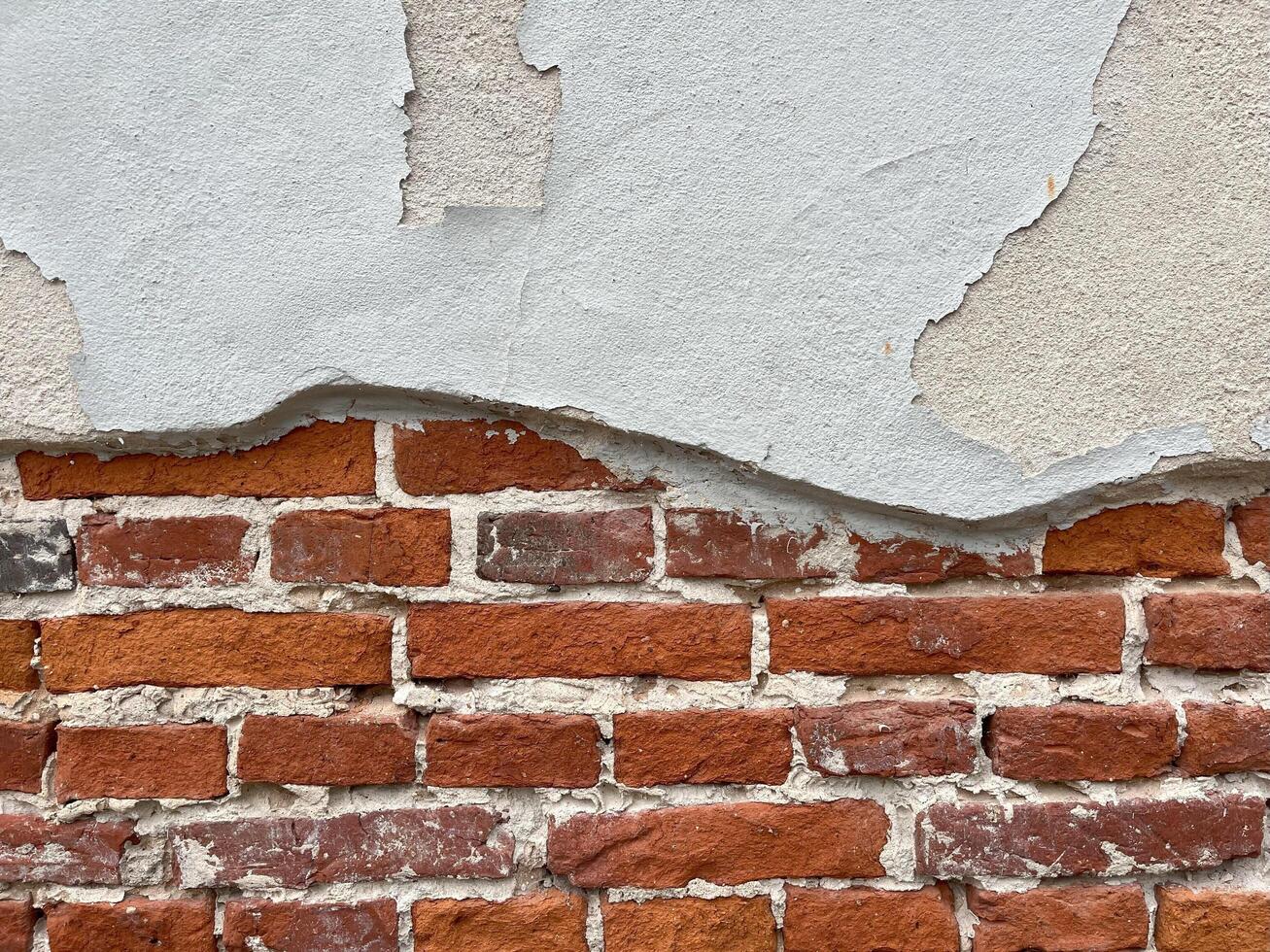 Texture of an old brick wall with fallen plaster and peeling wall paint. Background of a shabby building surface photo