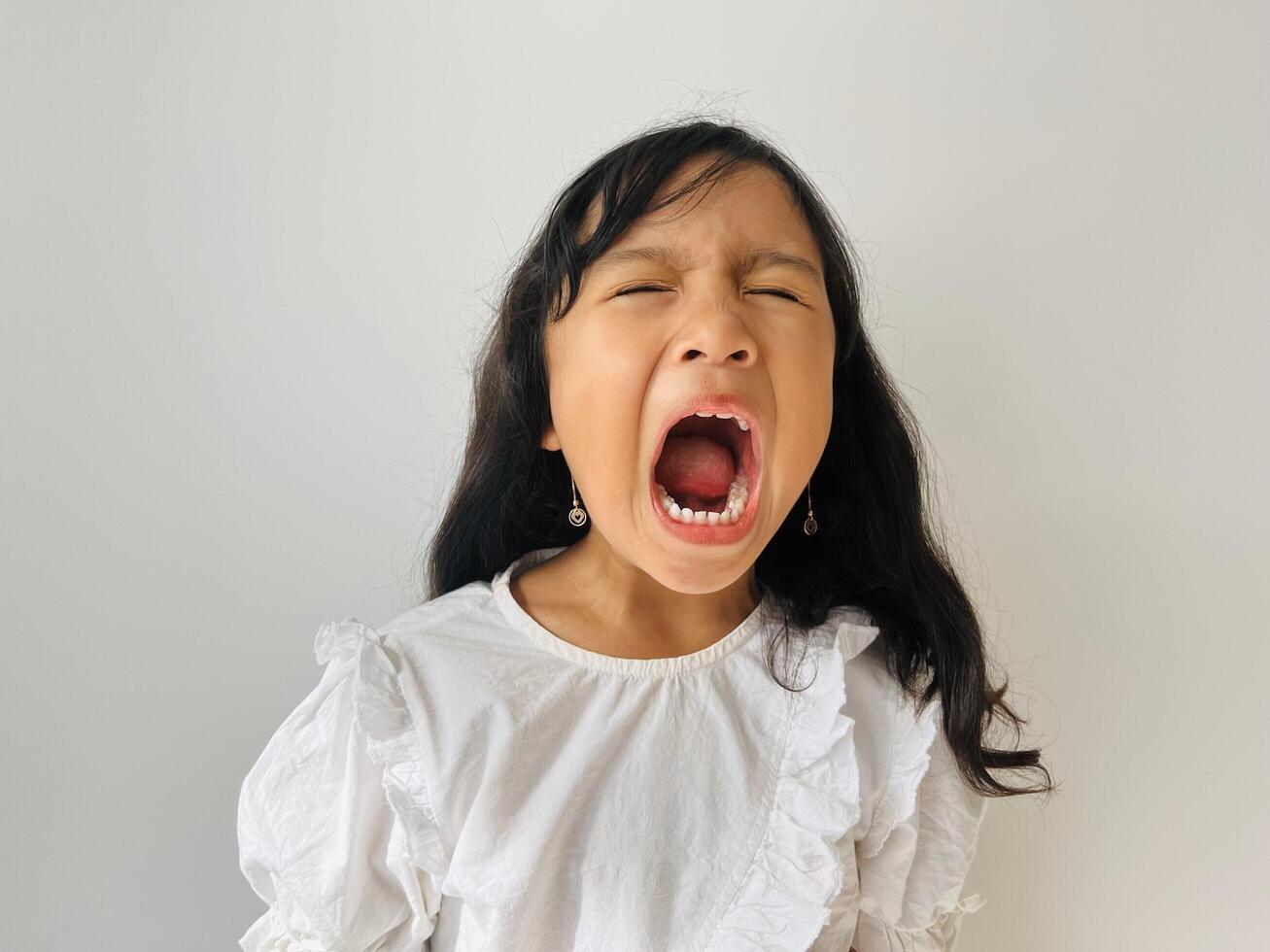Asian little girl 5 year old is open wide the mouth and close the eyes. Standing but sleepy little girl on white background photo