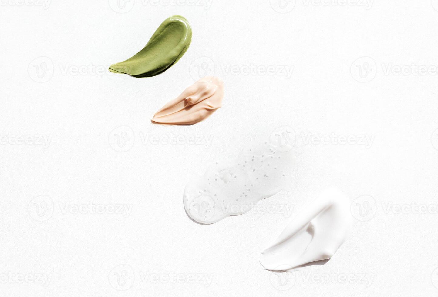 Cosmetic smears of green, pink and white colors cream on bright background. Various textured smear paint of cosmetic products on a white backdrop. Concept of health and skin care. Top view. Copy space photo