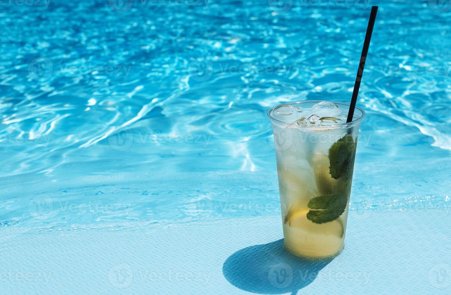 Delicious ice drink with lime, lemon and mint on the side of the pool. Tasty fresh mojito on the background of clear blue water. photo