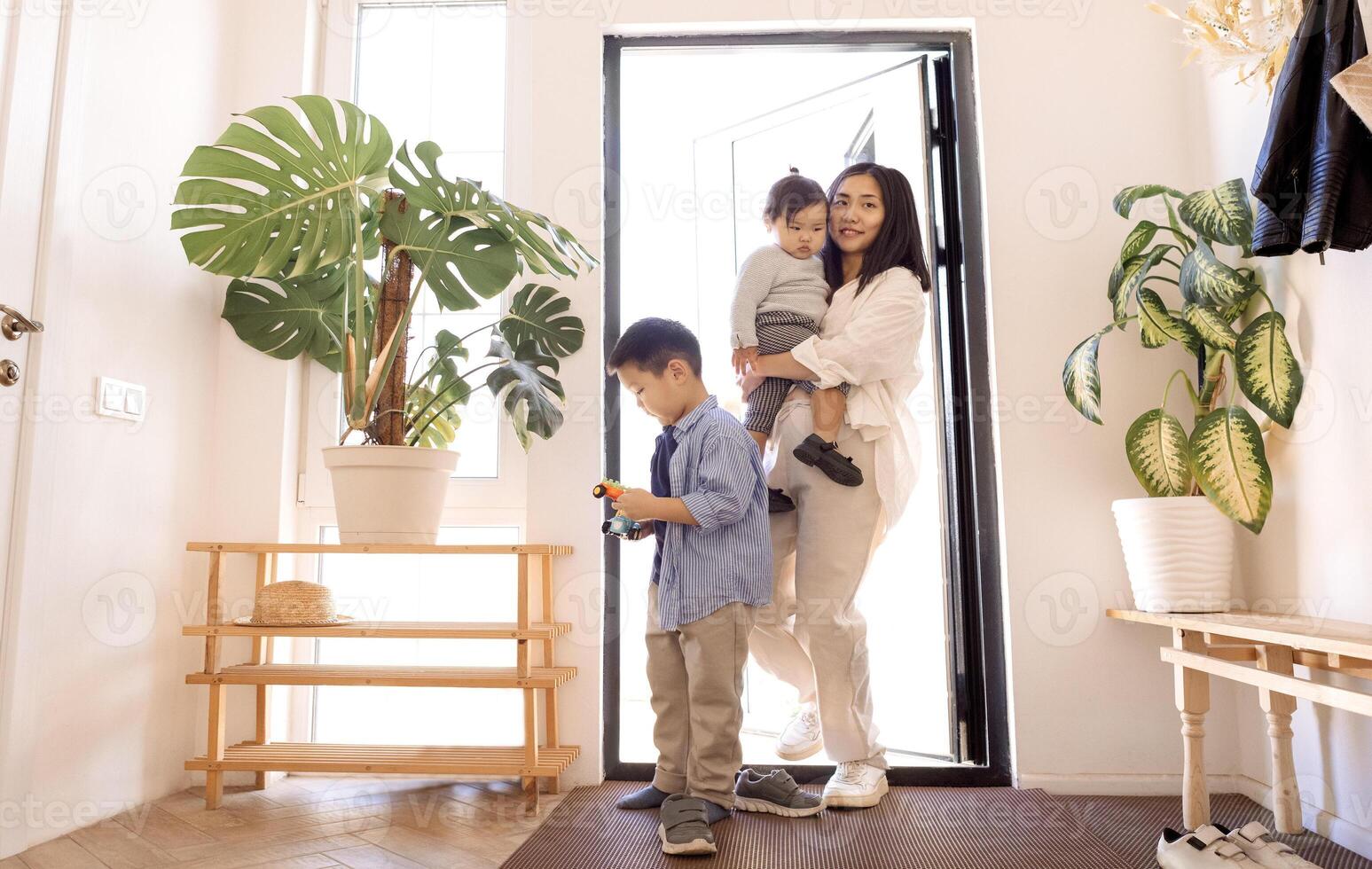 A happy Asian family. A young attractive woman helps to take off her little daughter shoes photo