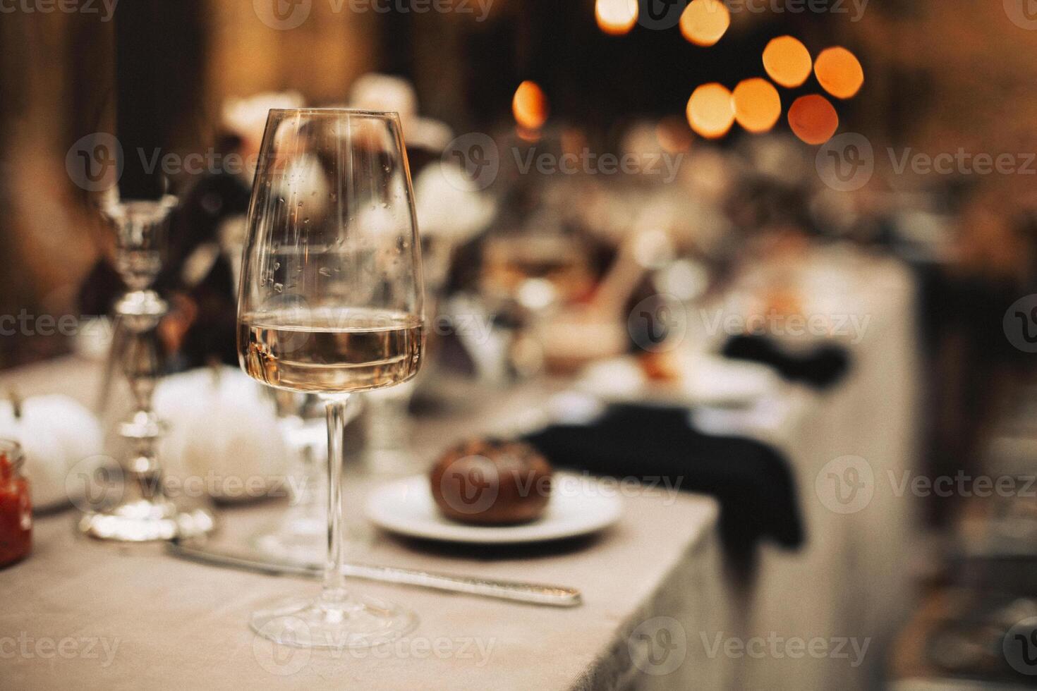 Selective focus on tall glass with white wine standing on dinner table after festive banquette photo