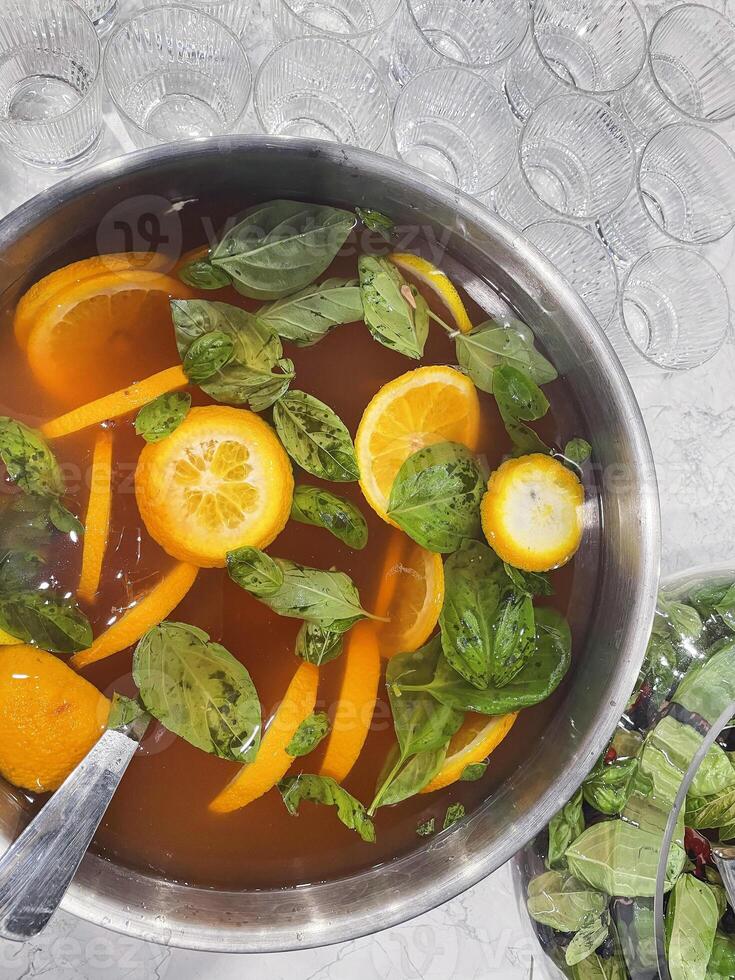 Punch large bowl with oranges and mint. Boiled citrus juice. Drink with a variety of fruits close up. Orange alcoholic cocktail. Empty glasses on the background table. photo