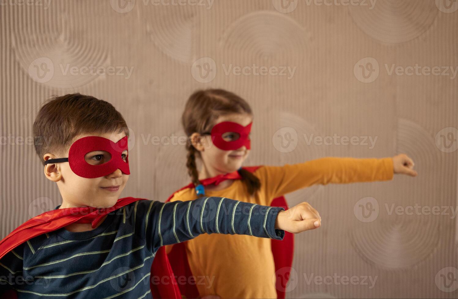 Portrait of a team of two young superheroes, brother and sister, over beige background photo
