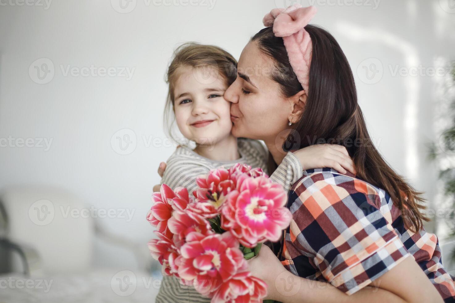 Smiling brunette mother hugging little daughter in cozy bedroom at weekend celebration Happy Mothers Day photo