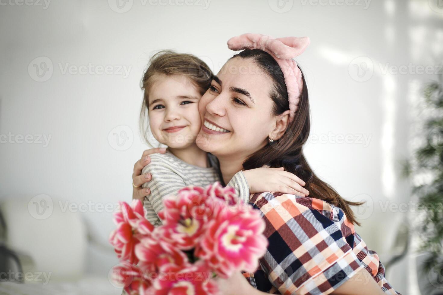 Smiling mother hugging little daughter in cozy bedroom at weekend celebration Happy Mothers Day photo