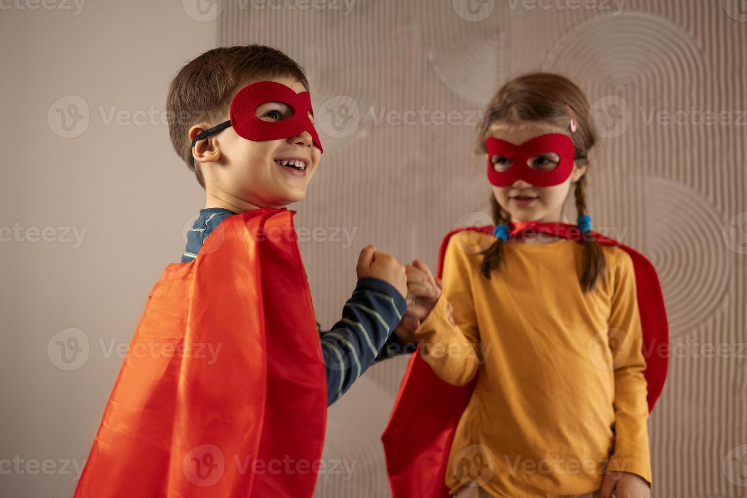 Portrait of a team of two young superheroes, brother and sister, over beige background photo