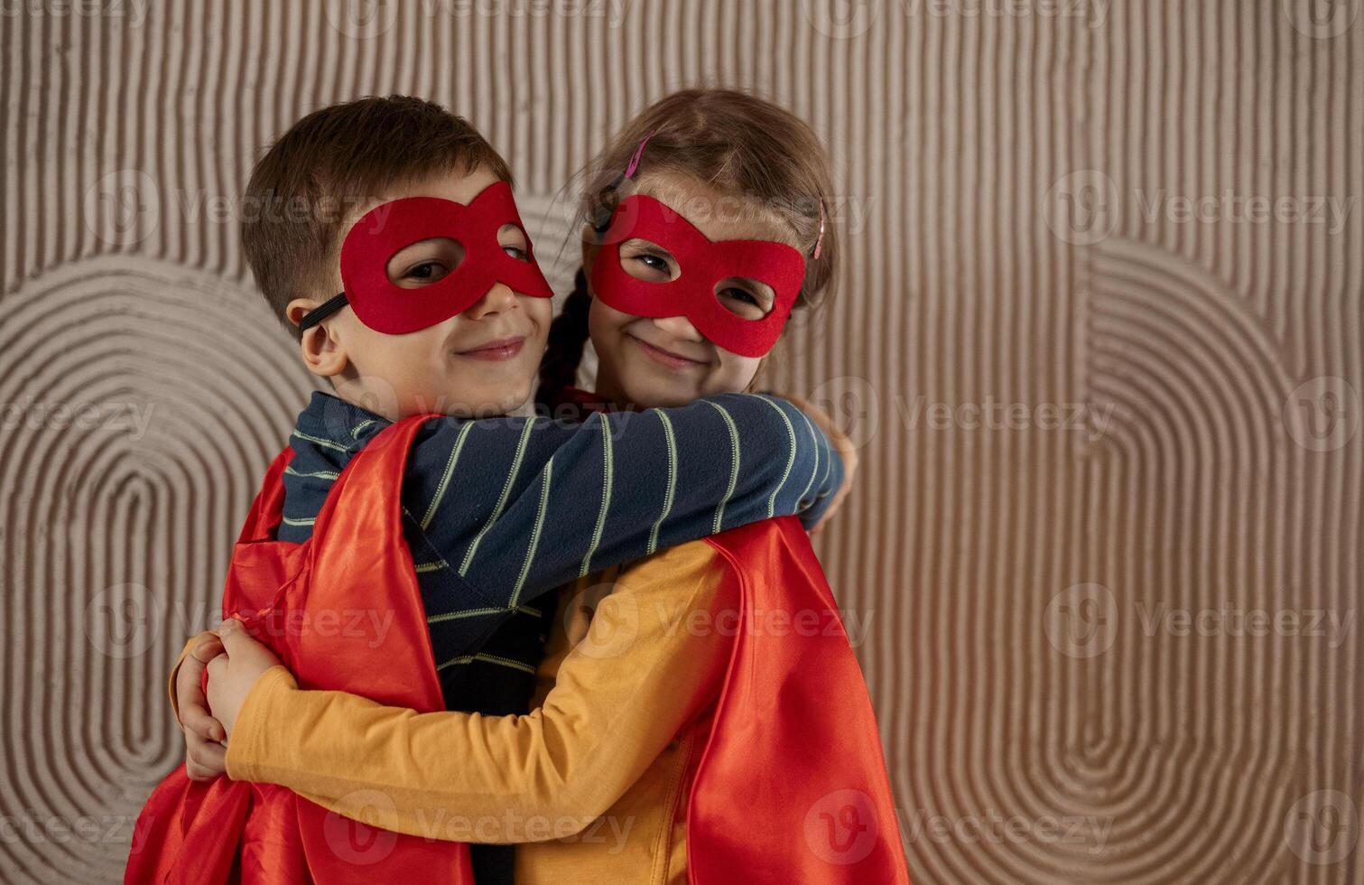 Portrait of a team of two young superheroes, brother and sister, over beige background photo