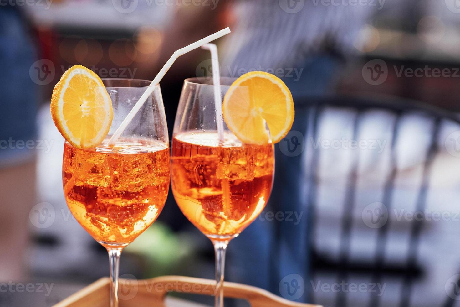 Two elegant champagne glasses on a long stem on a tray. Sparkling wine in cups for two on the table inside. Tasty alcoholic drinks with lemon slices and straws. photo