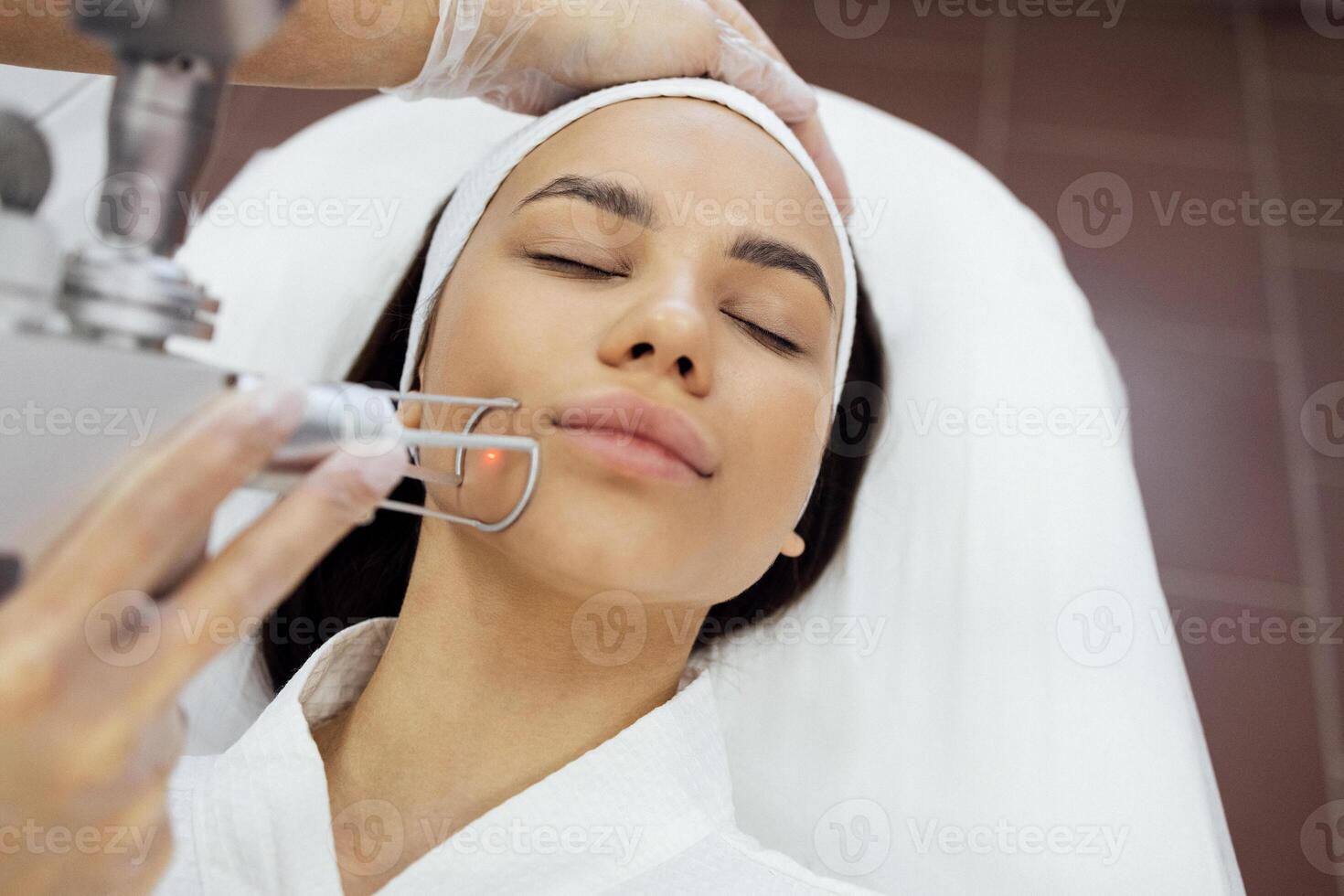Closeup of the face of young woman undergoing laser resurfacing and peeling procedure in spa salon. photo