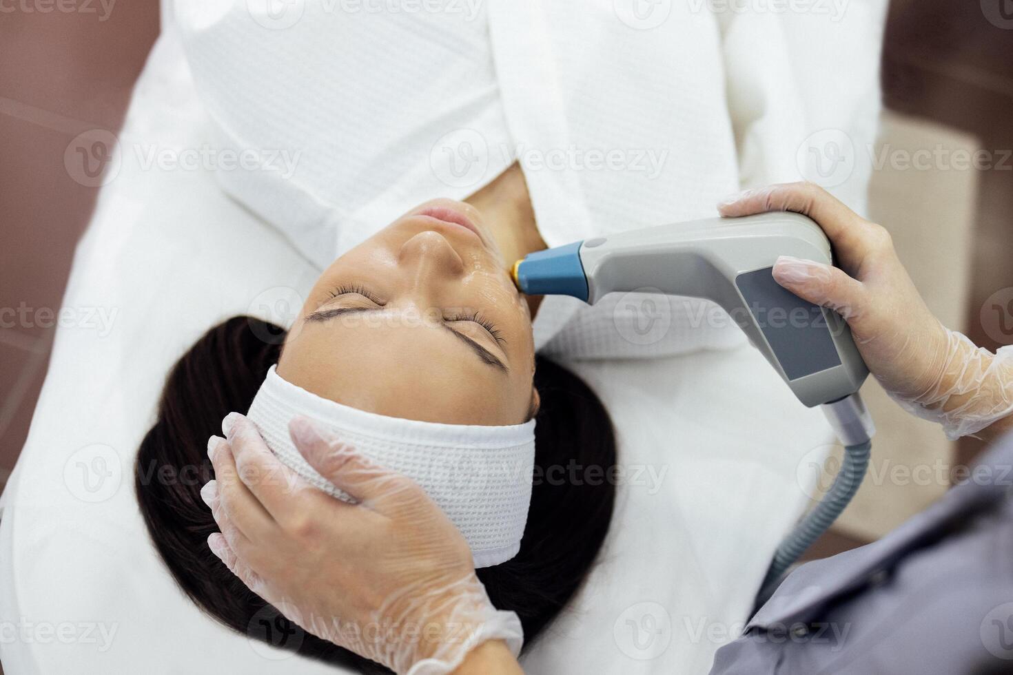 Cosmetologist in grey uniform and transparent gloves makes facial cleansing procedure for her young client photo