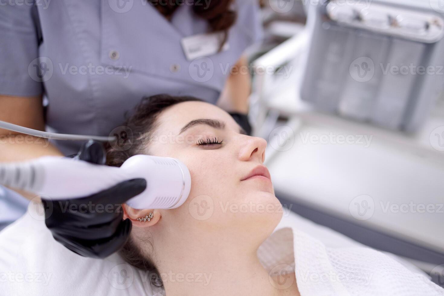 A young woman in a bathrobe lies and receives a facial cleansing procedure using a device photo