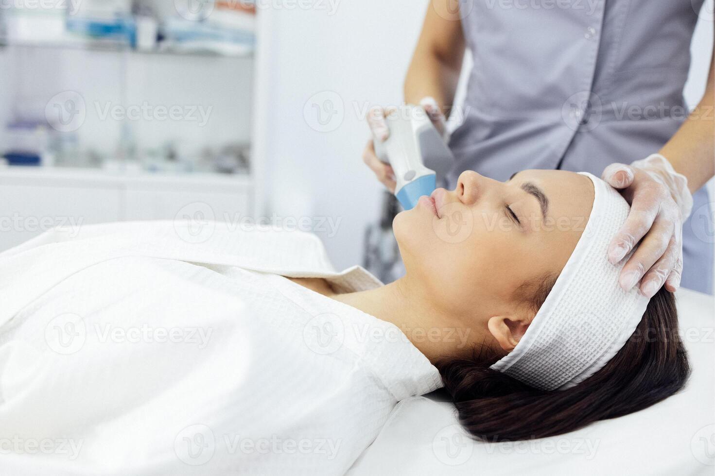 Cosmetologist in grey uniform and transparent gloves makes facial cleansing procedure for her young client photo