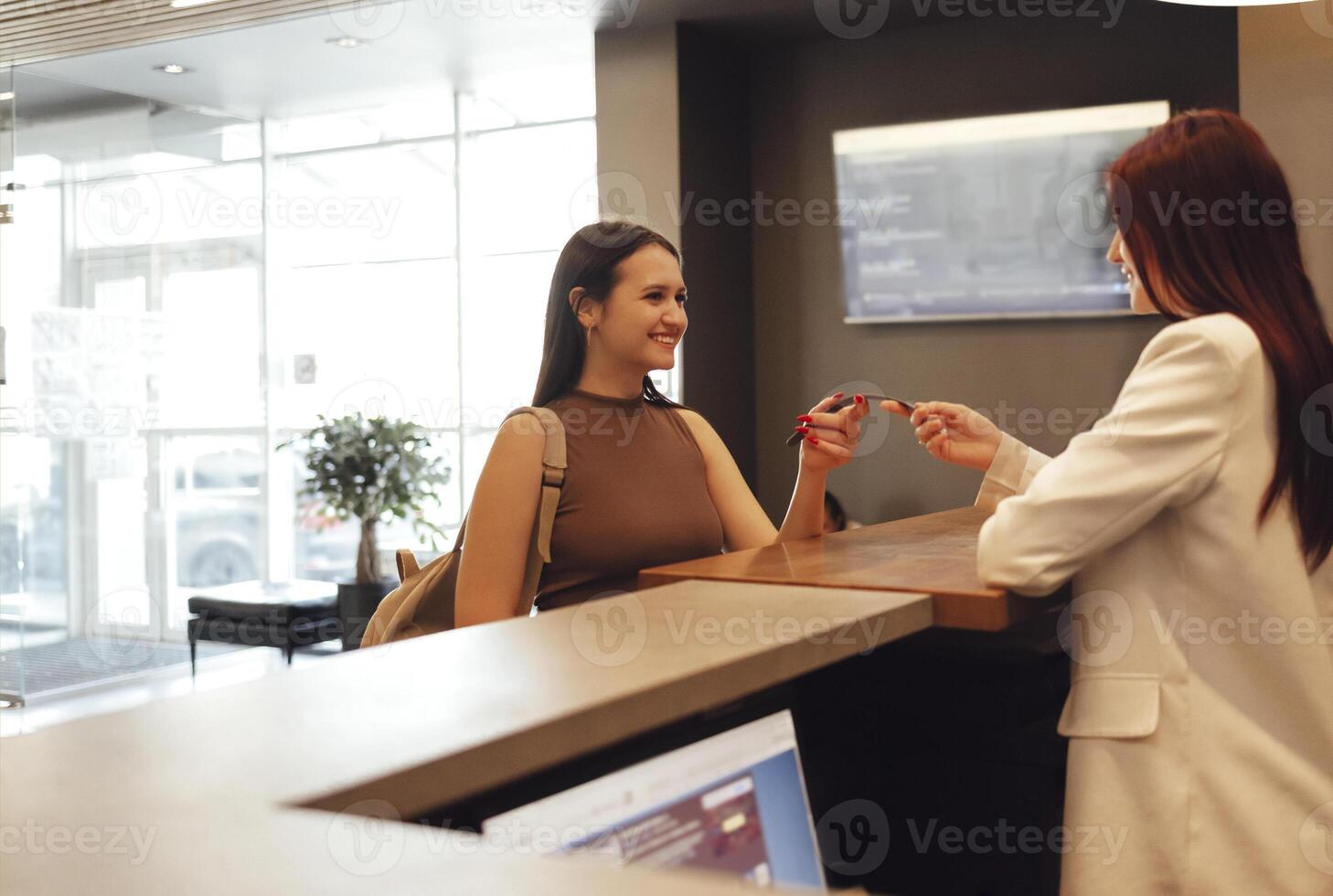Woman in sportswear taking the sport bracelet while standing in front of window at gym at reception area photo