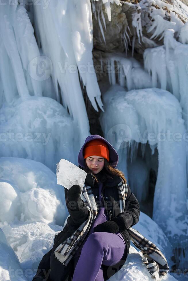 Girl with a beautiful radiant smile in sunny winter weather and red hat is holding an icicle from Lake Baikal photo