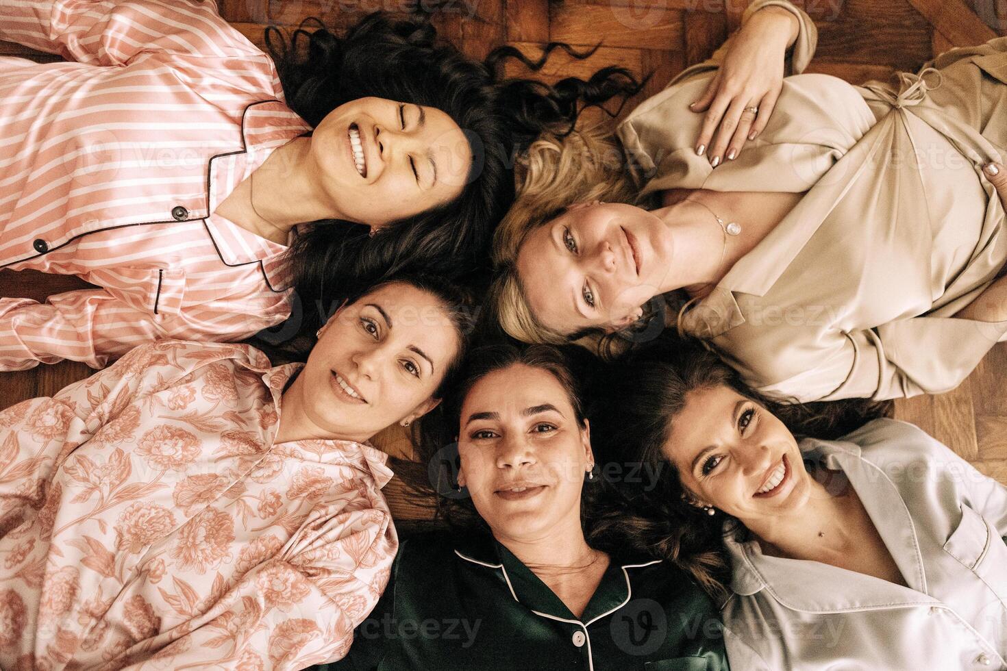 Young smiling women in pajamas are lying on the floor. Charming multiethnic friends at a house party. photo