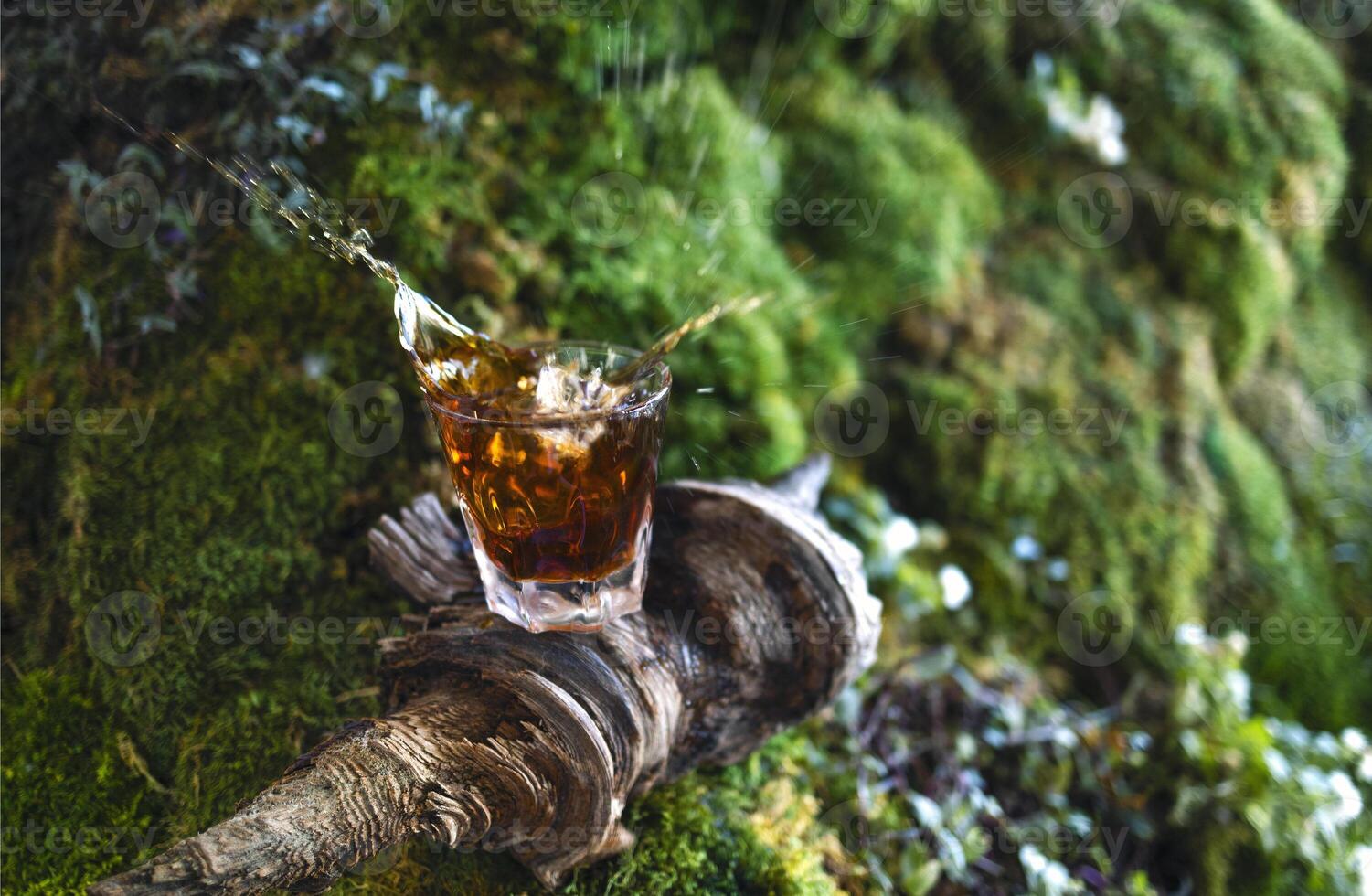 Whiskey glass on the wooden stick with nature green grass background photo