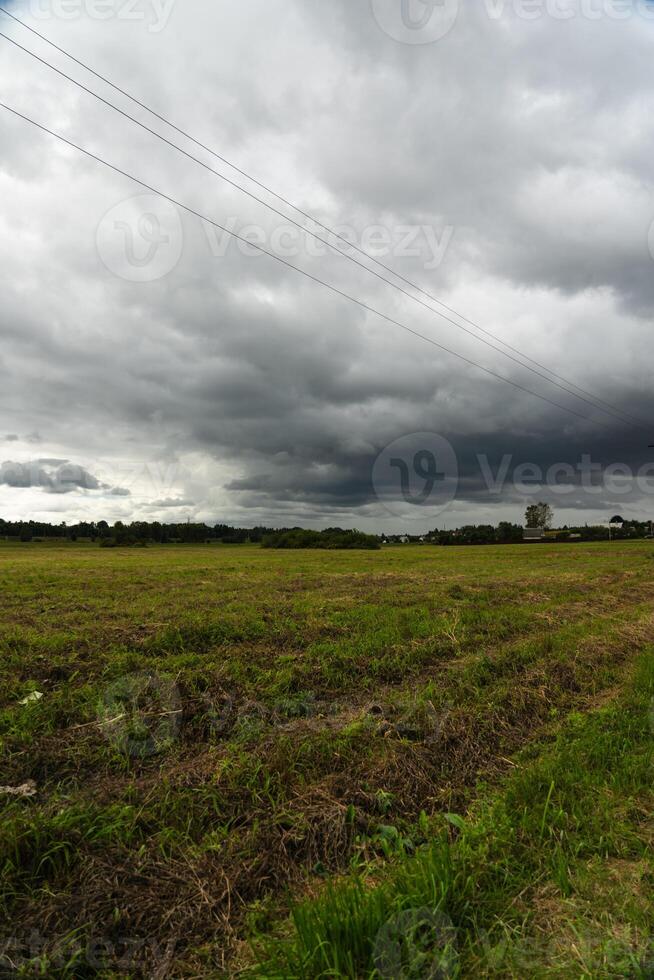 Clouds hung over the village and the green field. Support of power lines nearby photo