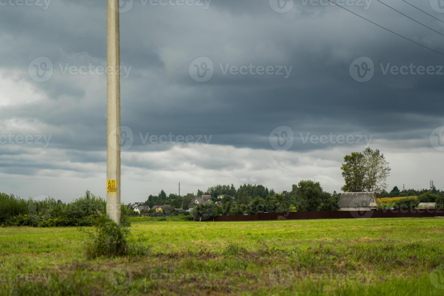 Clouds hung over the village and the green field. Support of power lines nearby photo