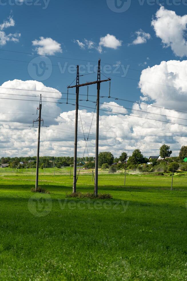 Supports of power lines in a green field. Clouds float across the sky photo