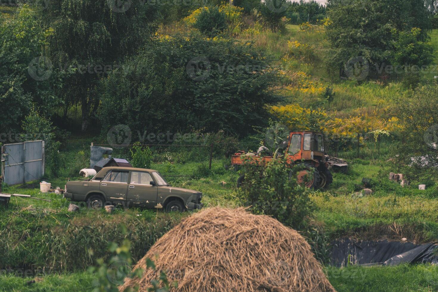 A rustic courtyard. A haystack. In the background is an old car and a tractor photo