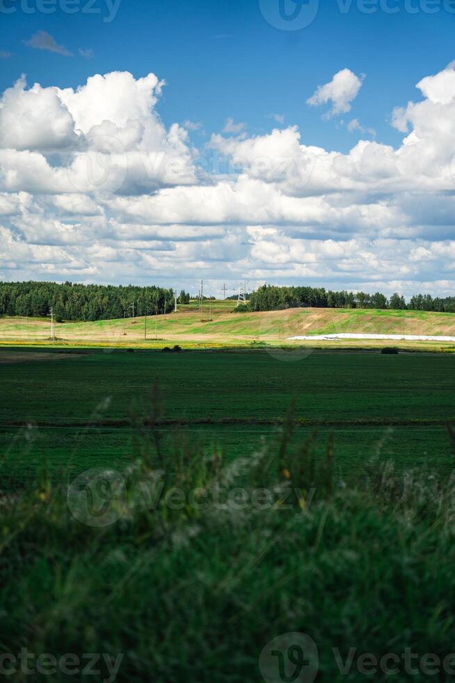 Thick clouds over green fields. The highway is far beyond the field photo