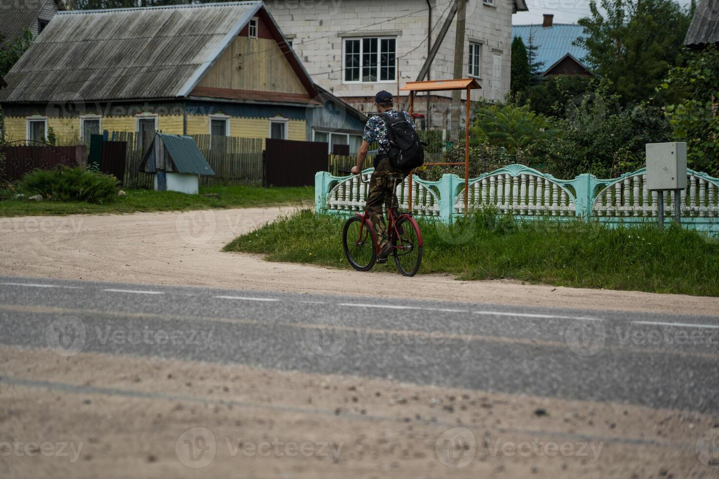 A village man rides a bicycle through the village with a briefcase on his back photo