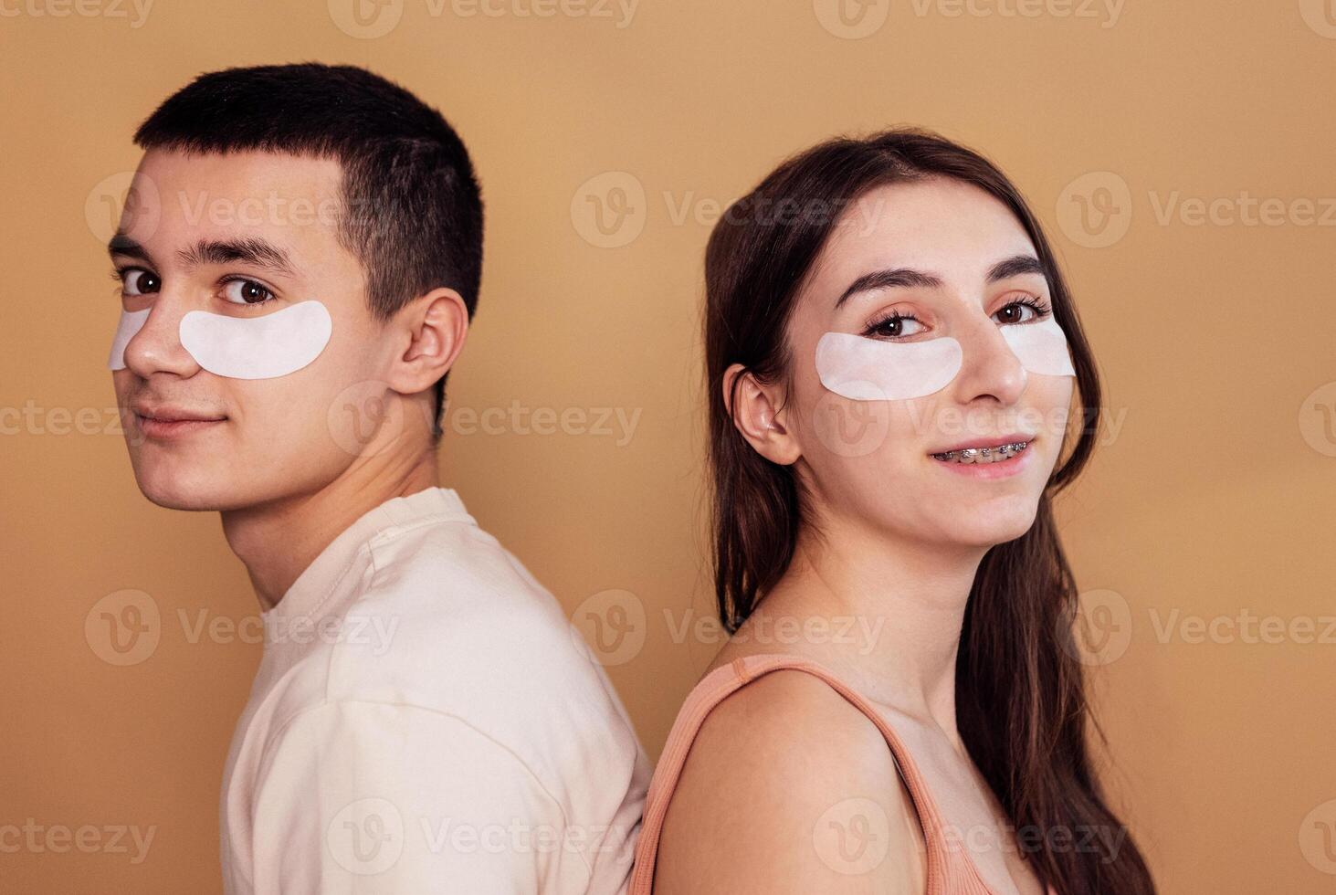 A smiling teenage couple with moisturizing patches under their eyes. A cute girl with braces and a boy take care of the skin of the face. Cosmetic procedure. Beauty routine. photo