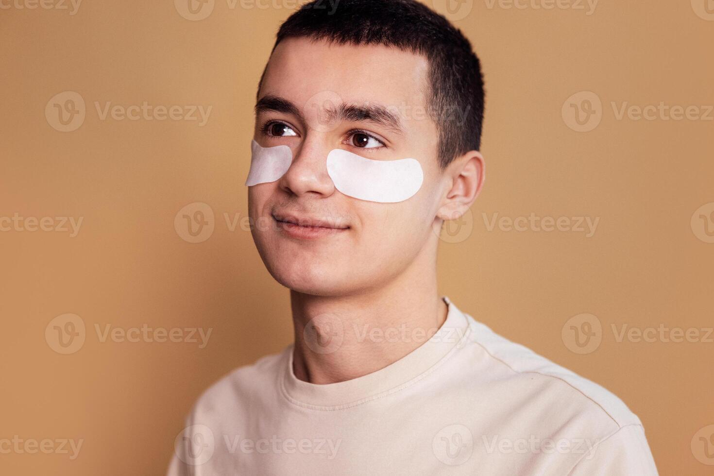 A close-up portrait of teenager with moisturizing patches under his eyes. Smiling boy take care of the skin of the face. Cosmetic procedure. Man beauty routine. photo