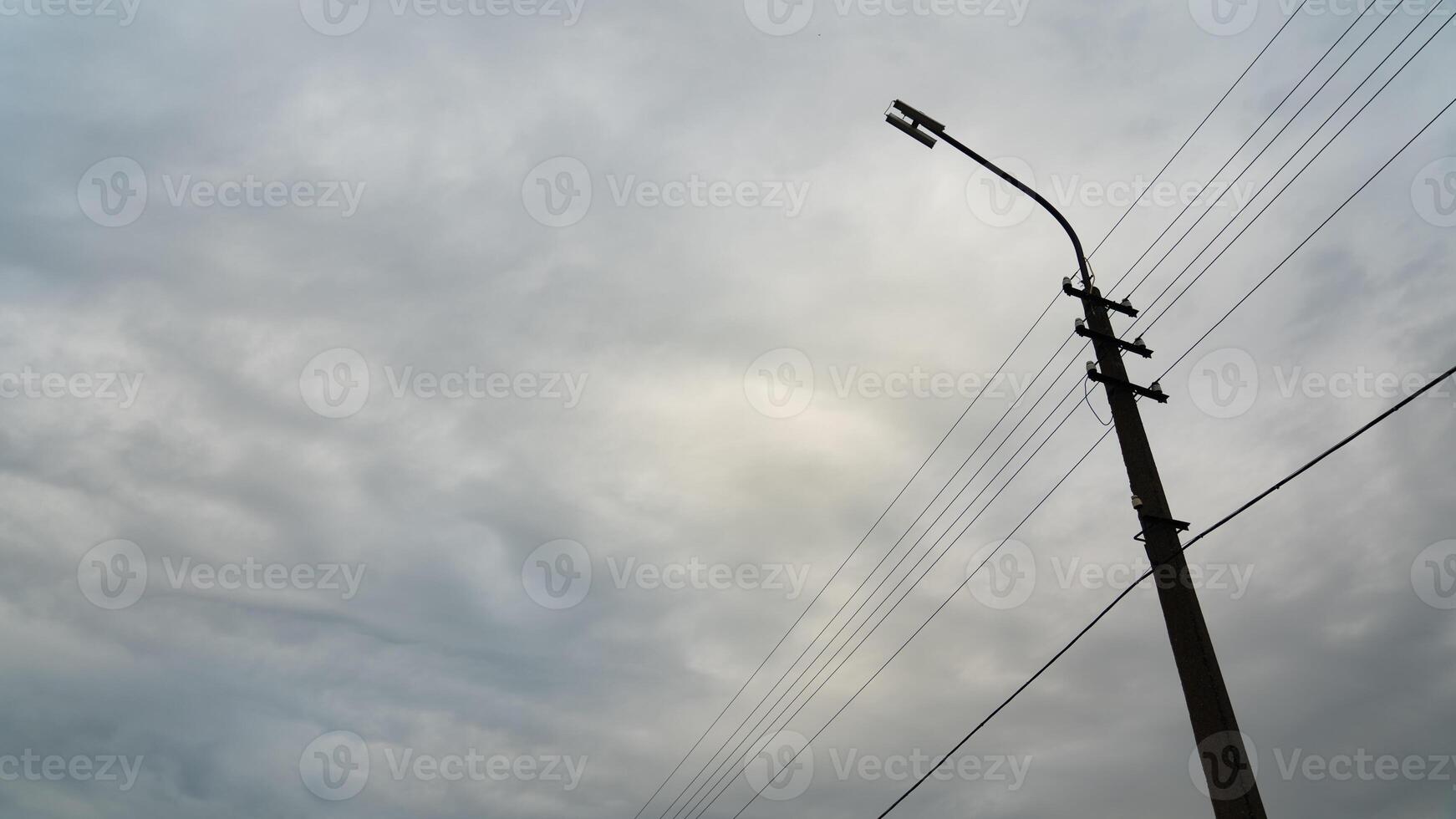 A lamppost with wires on the background of a cloudy dense sky. Grey, cloudy weather photo