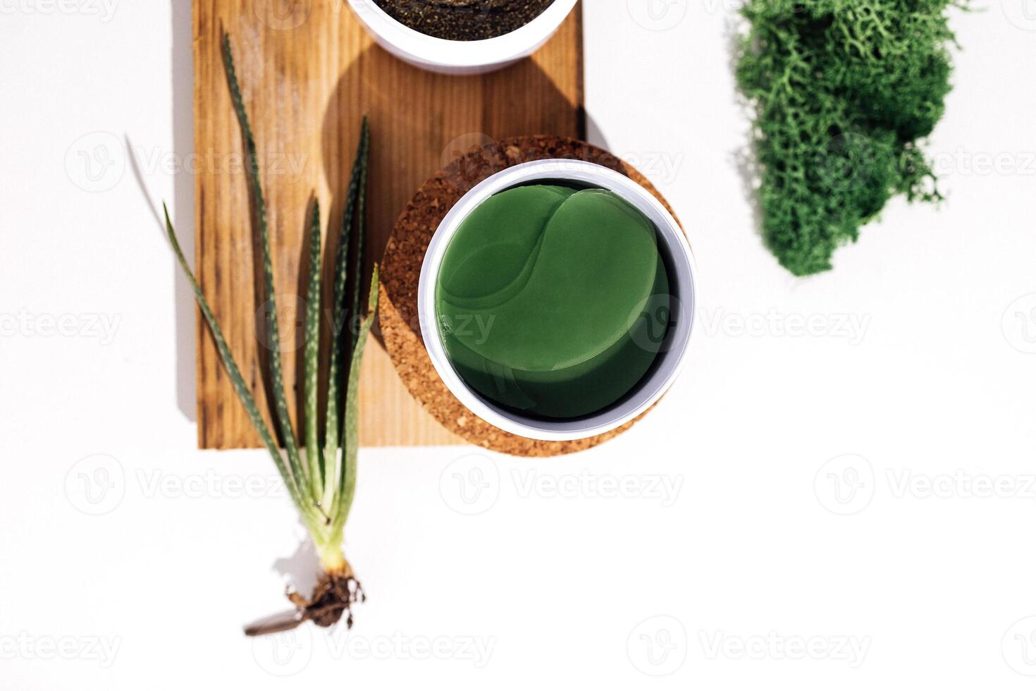 Plastic jar with green collagen eye patches on a cork stage. Aloe plant, wooden shap and moss on background. photo
