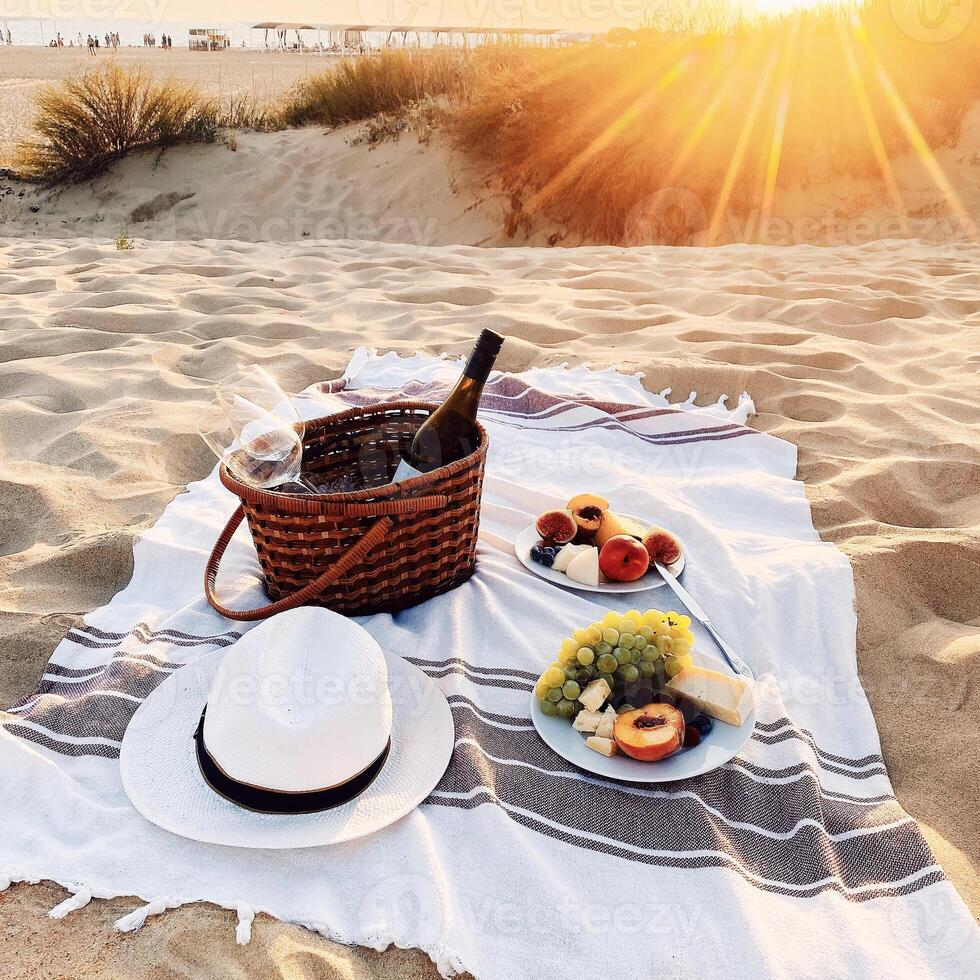 Romantic picnic with wine on sandy beach at amazing evening sunset photo