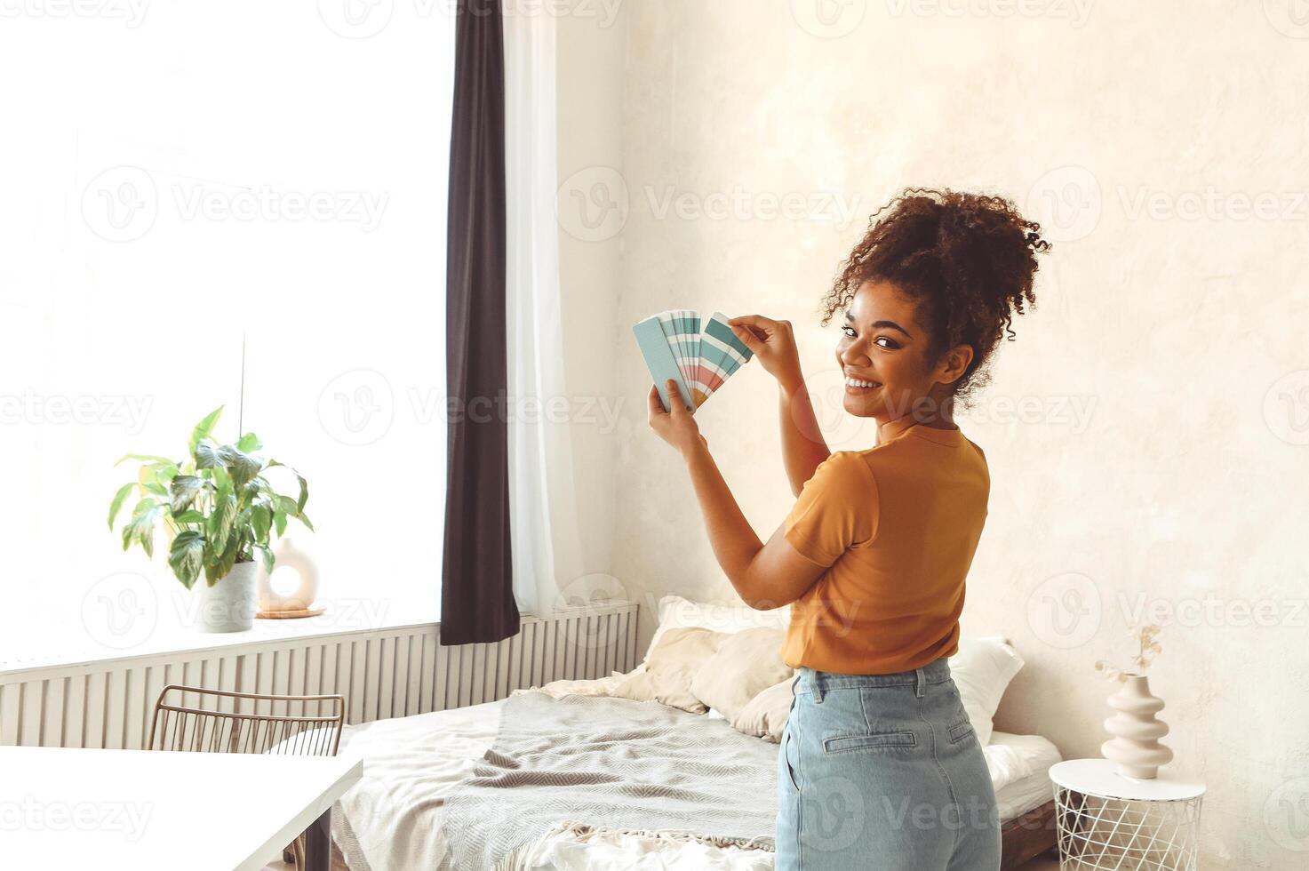 Smiling African American girl stands back to camera in middle of bedroom with paint color palette photo