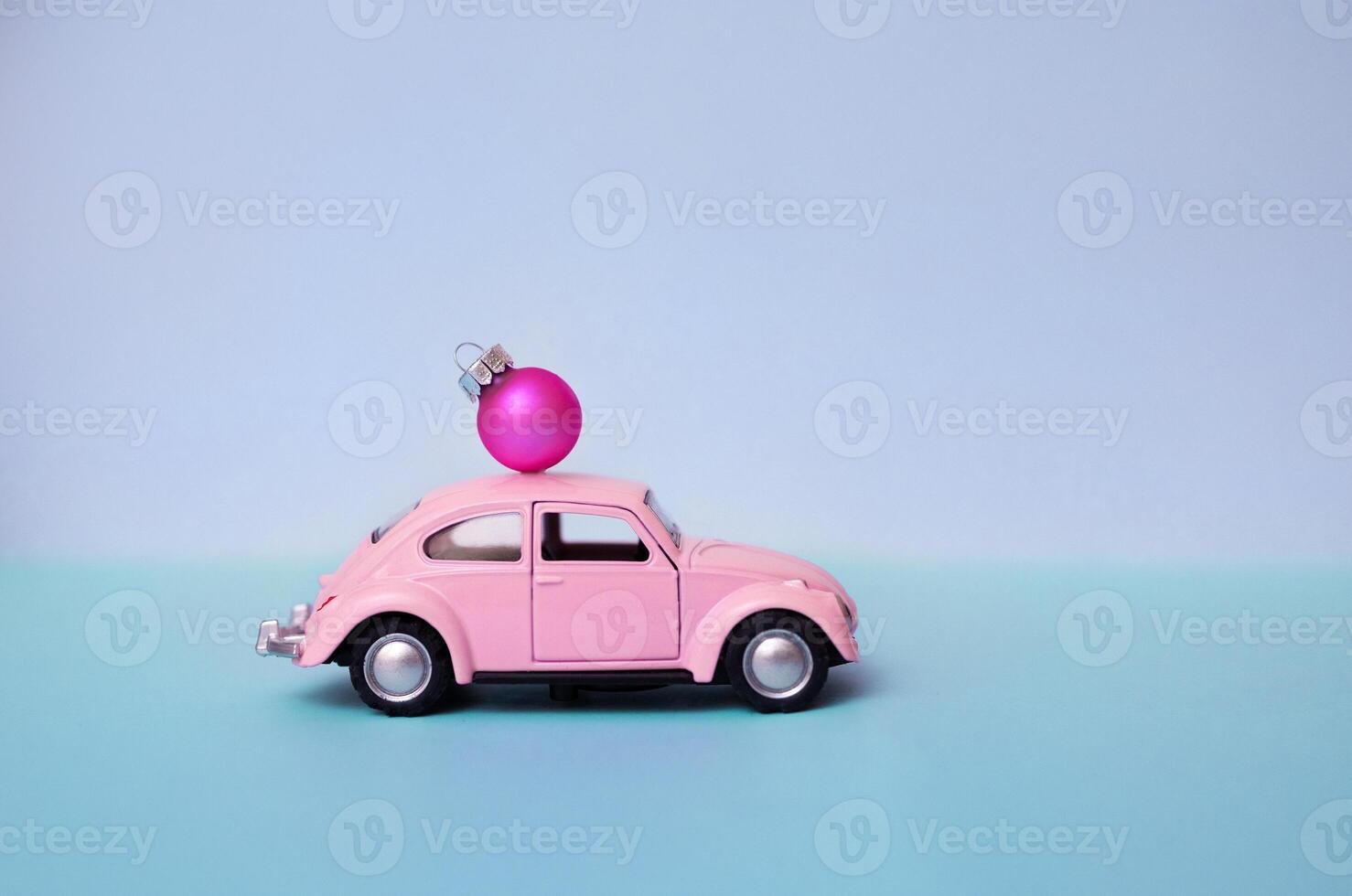 Pink toy car with a Christmas ball on the roof. Miniature automobile with a Christmas decoration on a blue background. photo