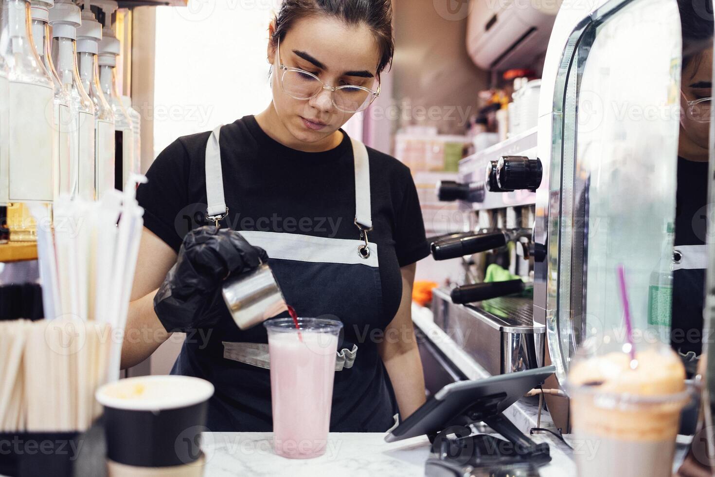 Young woman in black gloves prepares milky pink drink in street takeaway cafe photo