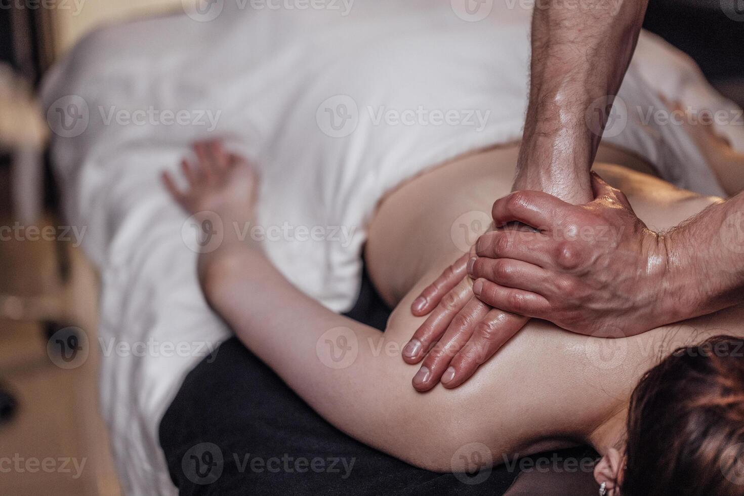 Happy young caucasian girl getting back massage in spa salon. Neat hands of male masseuse photo