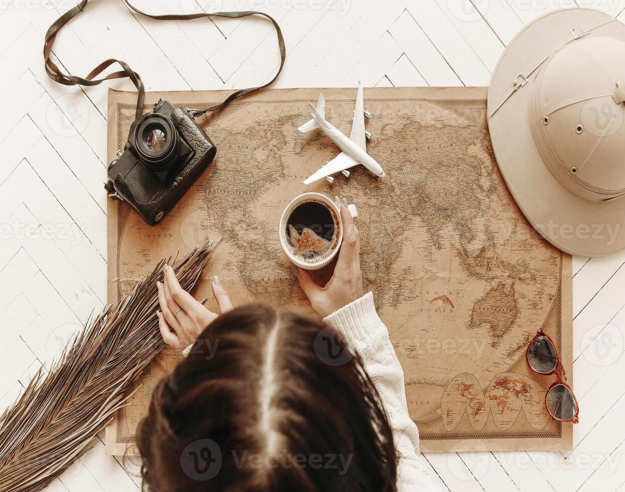 Top view of woman holds cup of black coffee over vintage world map with traveler accessories photo