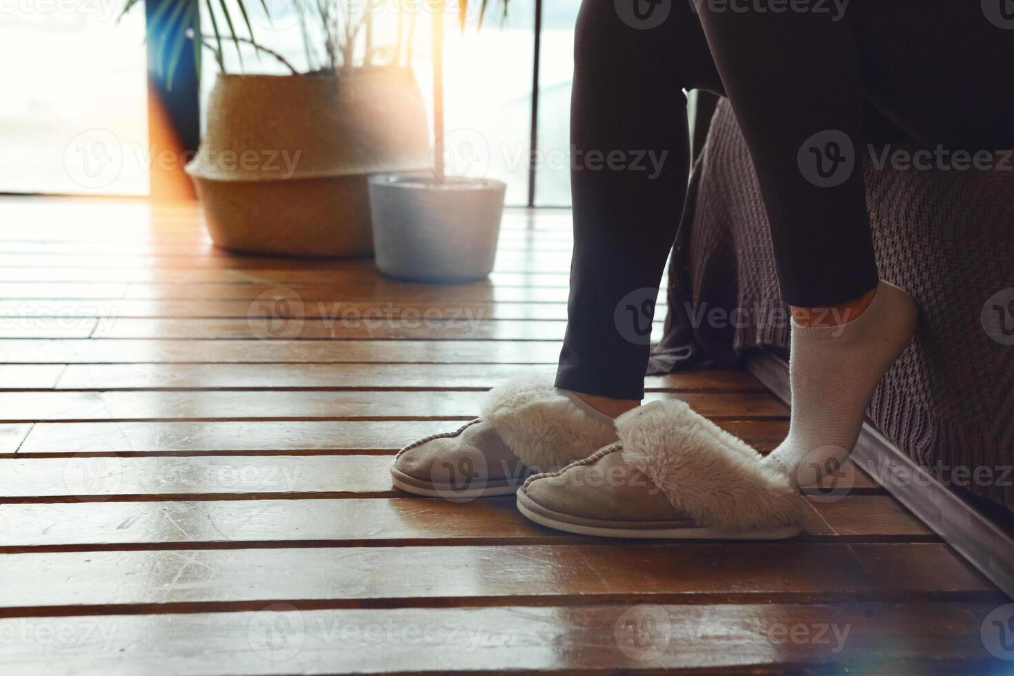 Woman putting on soft plush warm slippers while sitting on sofa at cozy home in cold season photo