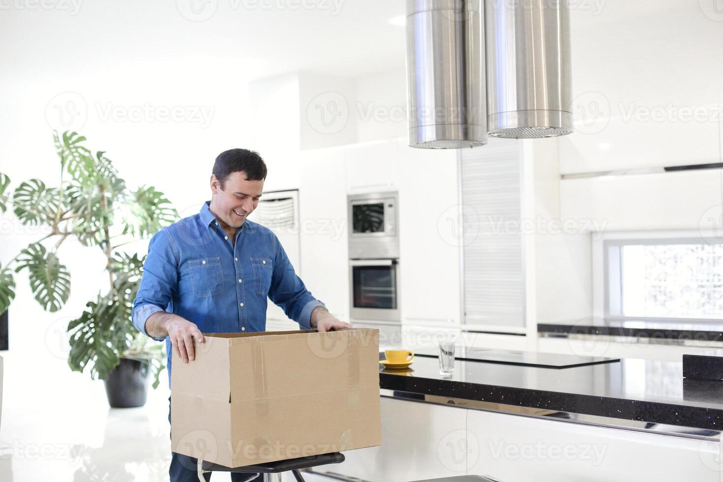 Young smiling brunette man unpacking box with kitchen tools at home photo
