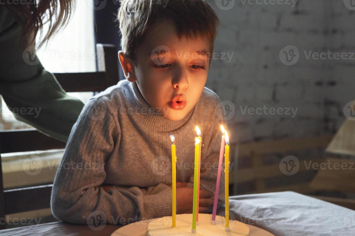 Little boy blowing out candles on homemade birthday cake during birthday celebration at home photo