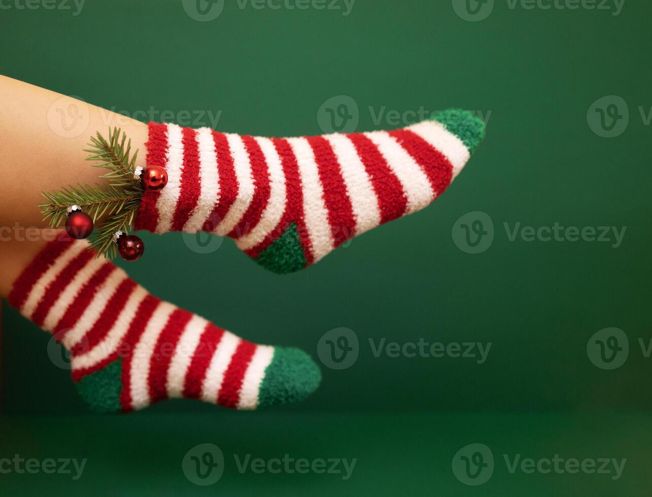 Gils feet in fluffy New Year warm socks. Christmas tree branch with balls decorats female leg photo